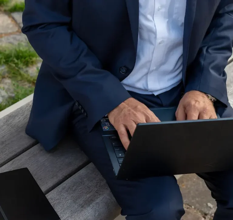 Person am Laptop Mann in Anzug sitzt auf einer Bank und tippt auf einem Laptop.